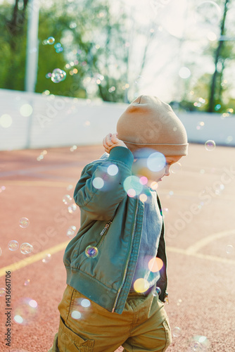 Obraz na płótnie Toddler boy running outside with soap bubbles. Child on a warm spring day for a walk in a jacket and hat. w salonie