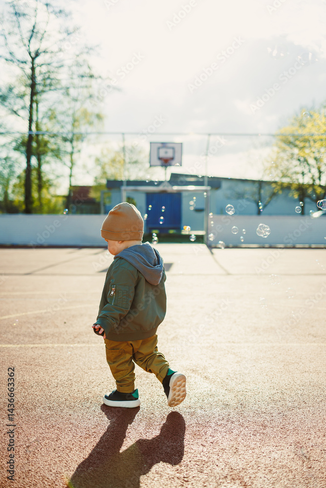 Cheerful 2 year old boy playing outside in summer in a green jacket with soap bubbles. Toddler boy running outside and playing with bubbles.
