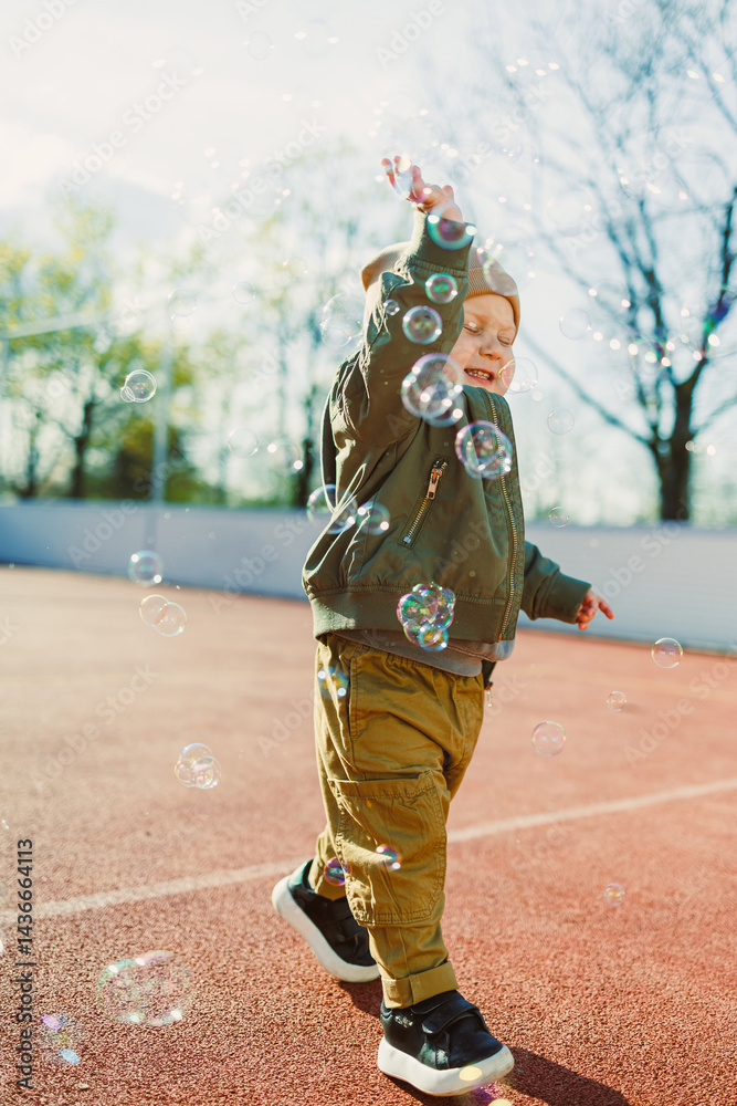 Little cute boy 2 years old running with soap bubbles. Boy catching soap bubbles in the park, enjoying a sunny summer day. Creative activities for children outdoors