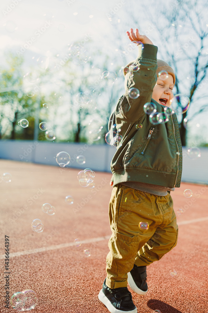 Little cute boy 2 years old running with soap bubbles. Boy catching soap bubbles in the park, enjoying a sunny summer day. Creative activities for children outdoors