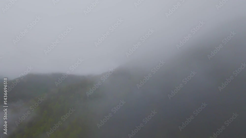 Aerial view of misty green mountains covered with lush forest, fog drifting through hills under a cloudy sky, creating a beautiful natural landscape perfect for travel, adventure, and nature tourism