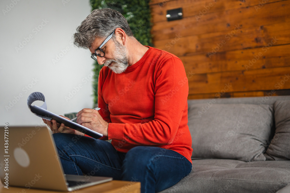 senior focused man work from home while use clipboard and laptop senior focused man work from home while use clipboard and laptop