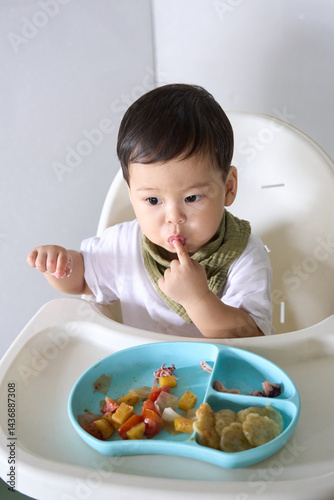 15 month old baby is sitting on high chair eating with fingers