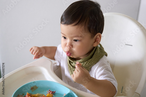 15 month old baby is sitting on high chair eating with fingers