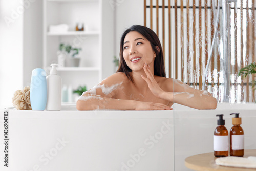 Obraz na płótnie Pretty young Asian woman with bottles of shower gel and loofah taking bath in bathroom w salonie