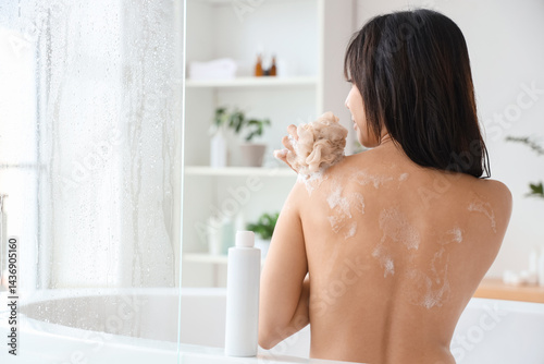 Fotografie Pretty young Asian woman with bottle of shower gel and loofah taking bath in bat