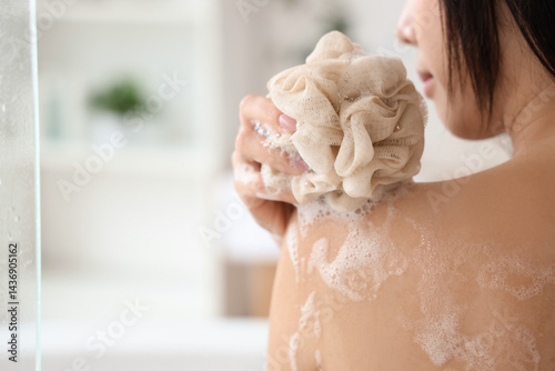 Фотография Pretty young Asian woman taking bath with shower gel and loofah in bathroom, clo