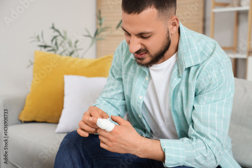 Young man with bandaged finger sitting on sofa at home