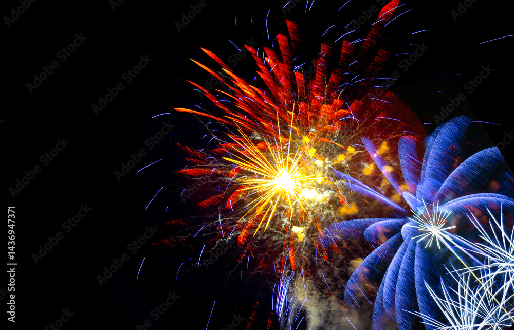 Brilliant orange, yellow and blue fireworks against a deep black night sky with copy space for festive or celebratory themes