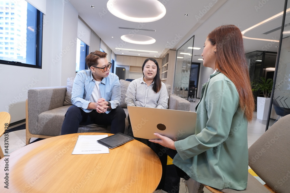 Asian female marketing and sales staff holding laptop explaining products to Asian male and female staff businessmen colleagues sitting in living room in company office and having discussion negotiati