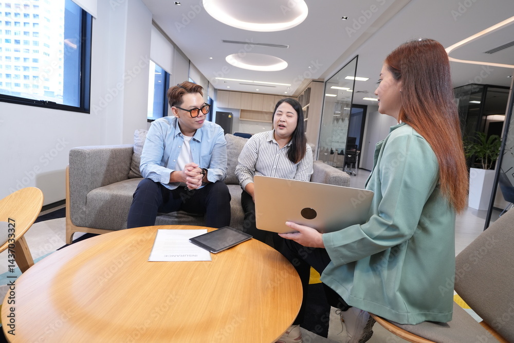 Asian female marketing and sales staff holding laptop explaining products to Asian male and female staff businessmen colleagues sitting in living room in company office and having discussion negotiati