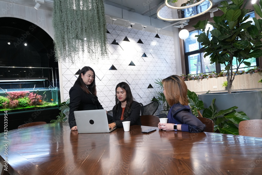 A group of three Asian female marketing colleagues discussing online sales and planning in a company conference room.