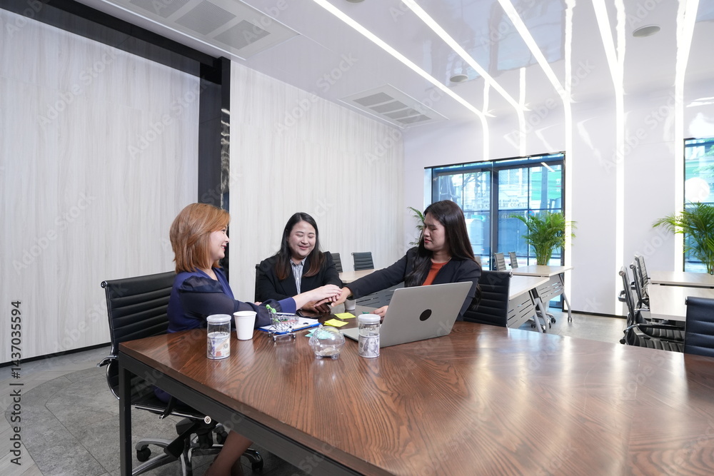 A group of three Asian female marketing colleagues discussing online sales and planning in a company conference room.