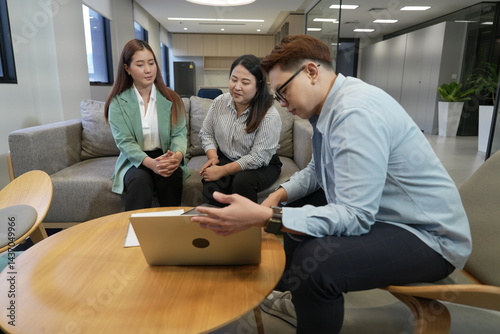 Obraz na płótnie An Asian male sales and marketing representative sits explaining information to two Asian female customers with a laptop in the company's living room.
w salonie