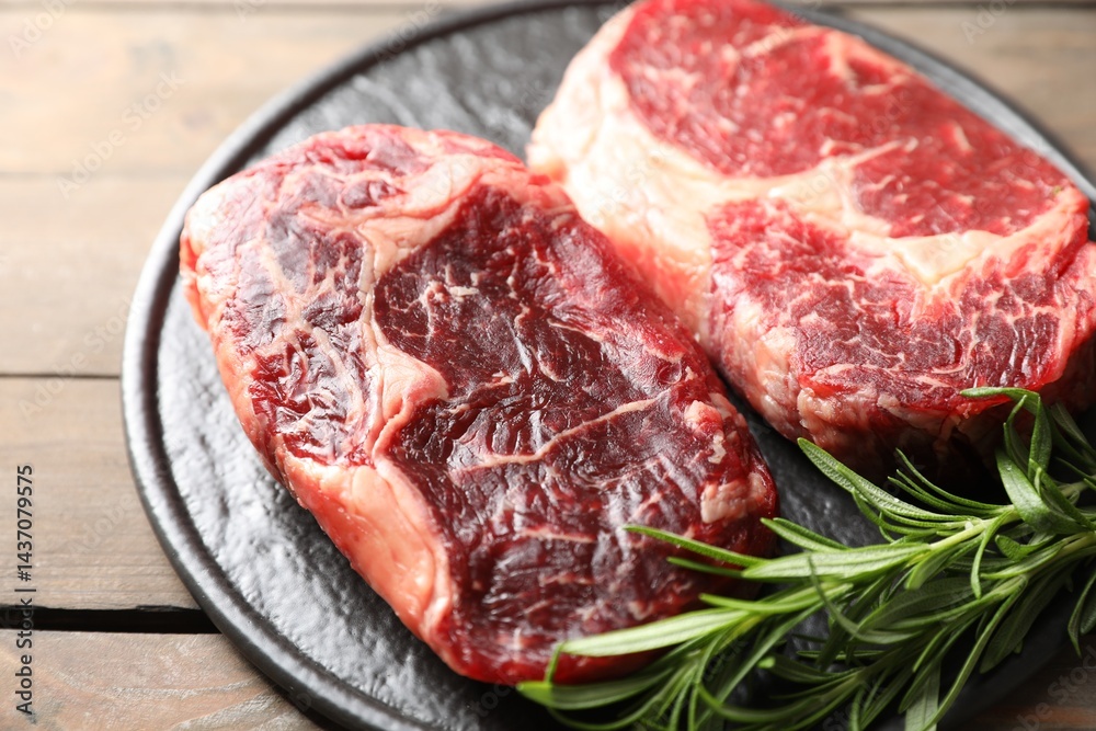 Fototapeta premium Pieces of raw beef meat and rosemary on wooden table, closeup