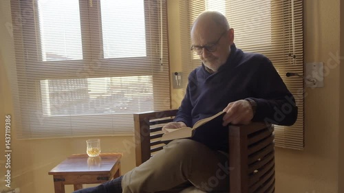 Elderly Man Relaxing Indoors with Whiskey and Book by Bright Window Light