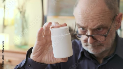 Elderly Man Examining Medicine Bottle While Wearing Glasses Indoors