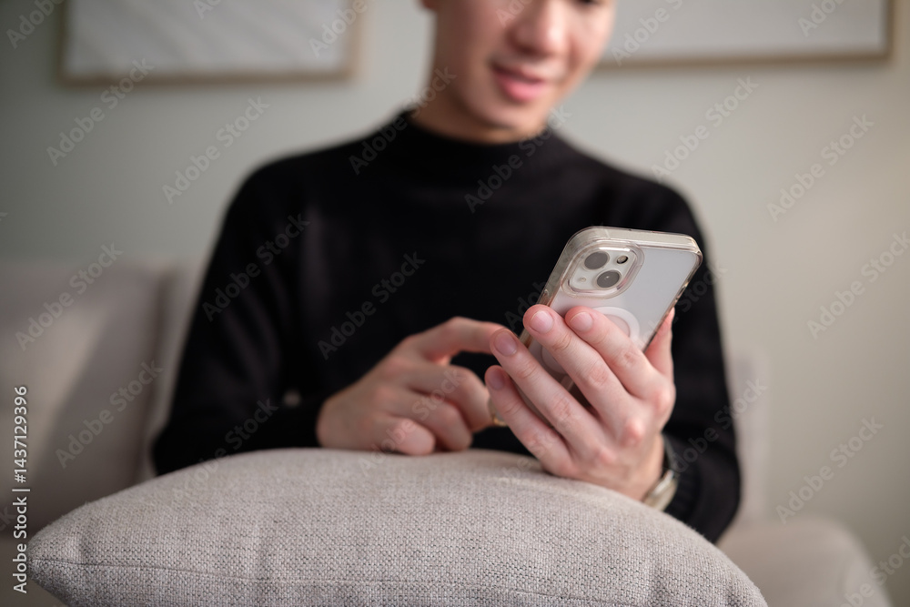 Close up of young man using smartphone while sitting on couch at home. Close up of young man using smartphone while sitting on couch at home.