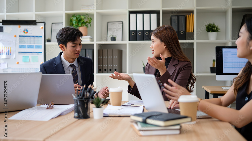 Business professionals engaged in active discussion around a table with laptops, documents, and coffee cups. Business professionals engaged in active discussion around a table with laptops, documents, and coffee cups.