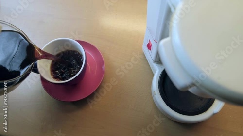 A man in a bathrobe pours freshly brewed coffee into an elegant cup with a stylish pink saucer.
