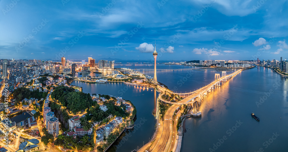 Fototapeta premium Aerial view of Macau skyline, bridge, and illuminated coastal road network at twilight, China.