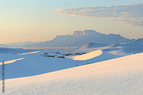 Sunrise over white desert landscape with distant mountain range  Soft light illuminates dunes and distant peak