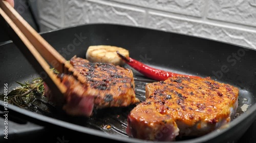 a chef fries a steak with rosemary and garlic in a frying pan. A chef flips a delicious steak with culinary tongs.