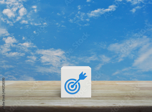 Target with dart flat icon on white block cube on wooden table over blue sky with white clouds, Business success concept