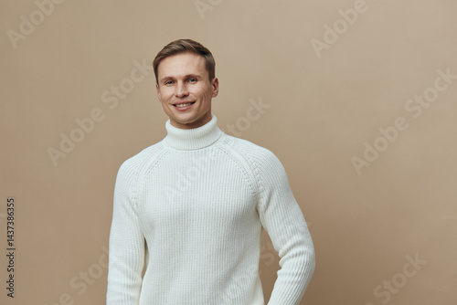 Tableau sur toile Smiling young man wearing white knitted turtleneck jumper pose on plain beige background studio portrait