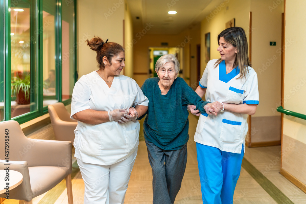 Nurses helping elderly woman walking in nursing home corridor