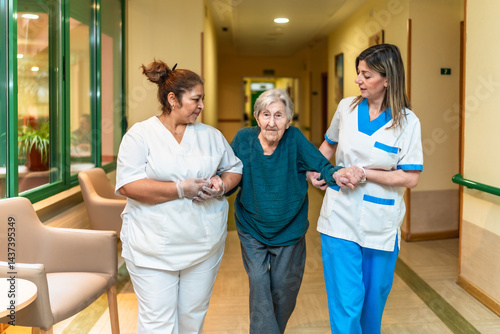 Obraz na płótnie Nurses helping elderly woman walking in nursing home corridor w salonie