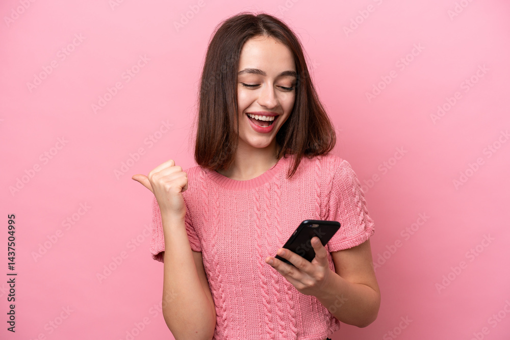 Young Ukrainian woman isolated on pink background using mobile phone and doing victory gesture Young Ukrainian woman isolated on pink background using mobile phone and doing victory gesture