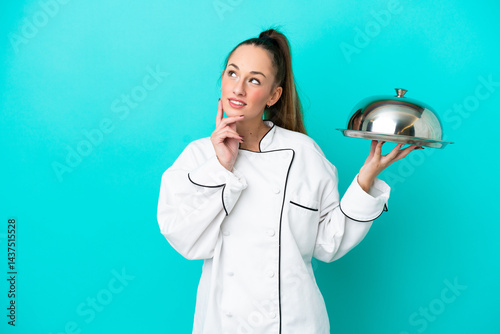 Young caucasian chef woman with tray isolated on blue background thinking an idea while looking up