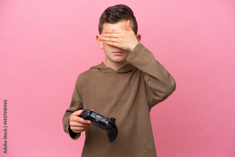 Little caucasian boy playing with a video game controller isolated on pink background covering eyes by hands. Do not want to see something Little caucasian boy playing with a video game controller isolated on pink background covering eyes by hands. Do not want to see something