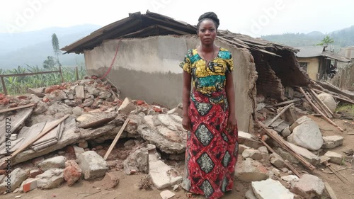 Woman stands in front of the ruins of a house damaged by natural disaster in rural area.
