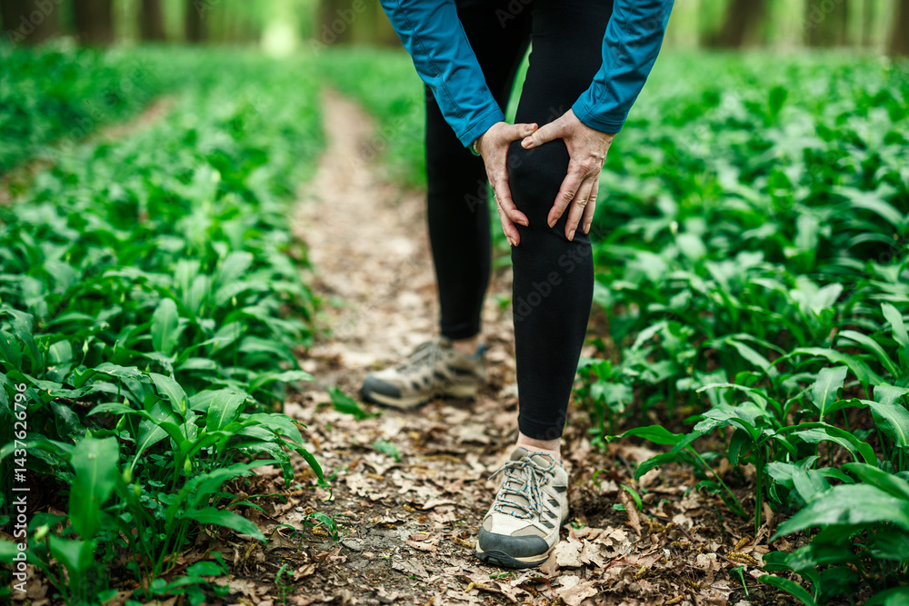 Woman runner holding knee in pain during forest run, concept of sport injury and joint strain