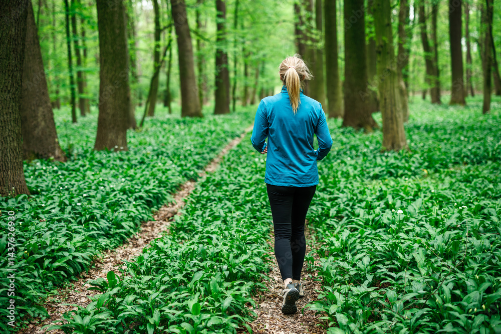 Woman running on forest trail. Female runner wearing sports clothing. Outdoor leisure activity