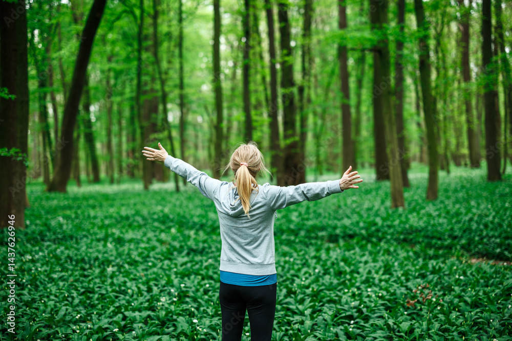 Woman athlete celebrating freedom with arms wide open in nature, symbol of relaxation and mental wellbeing. Forest bathing