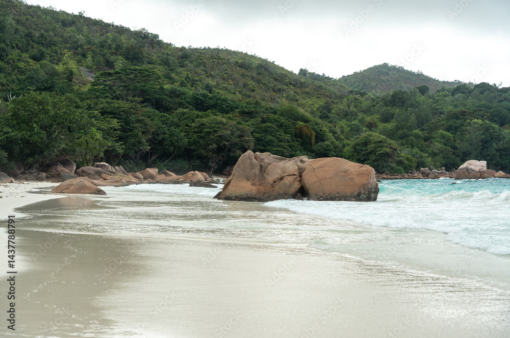 Tropical beach on Praslin island, Seychelles, with turquoise ocean waves, lush jungle hills