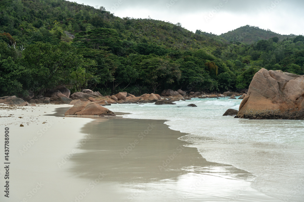 Tropical beach on Praslin island, Seychelles, with turquoise ocean waves, lush jungle hills