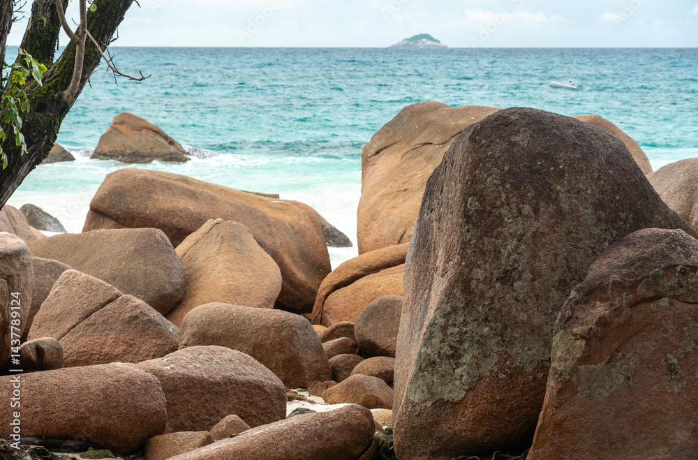 Massive granite boulders on a tropical beach of Praslin, Seychelles, with turquoise sea waves