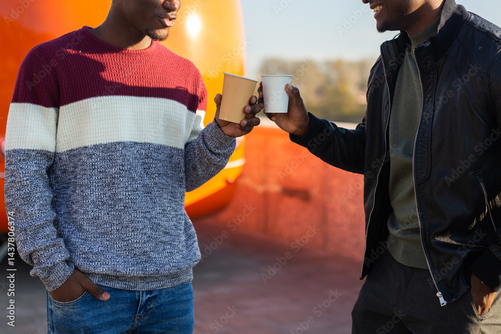 Two african american friends clink coffee cups on a sunny afternoon. Concept of friendship, connection, street lifestyle and casual communication.