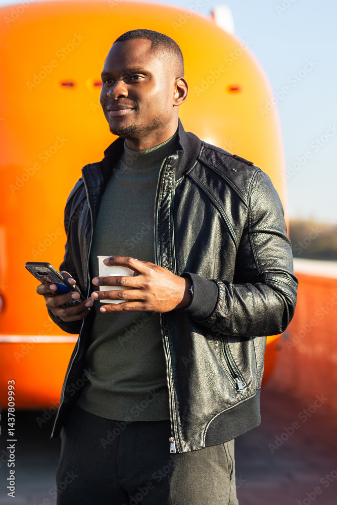 African american Man holding coffee and smartphone at a street food truck. Concept of travel, urban lifestyle and casual communication.