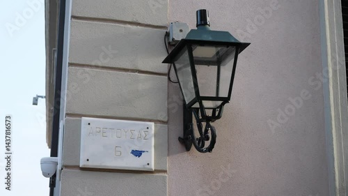 Close-up of a building corner with a vintage-style streetlight hanging nearby. A street sign with the name of the street in Greek is visible. Located in Athens, in the old town area
