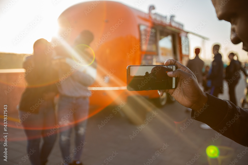 African american man photographing friends with smartphone near food truck. Concept of modern communication and leisure moments.