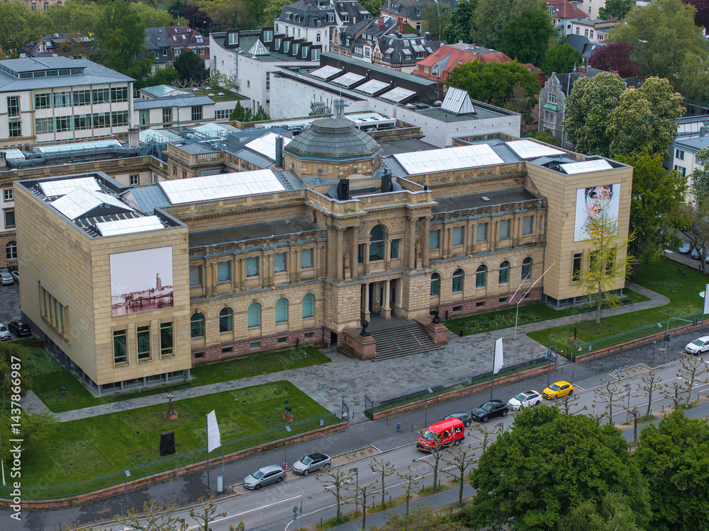 Aerial view of the Stadel Museum in Frankfurt, Germany, showcasing its neoclassical architecture, central dome, banners, greenery, and urban surroundings.