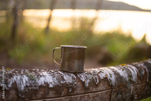 iron tourist mug with hot coffee on the log near a lake