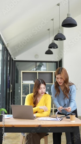 Two business women are sitting and talking in the office and discussing projects on laptops and graphs working together in the office.