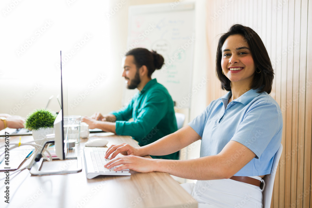 Fototapeta premium Smiling businesswoman typing on keyboard working in modern office with colleagues