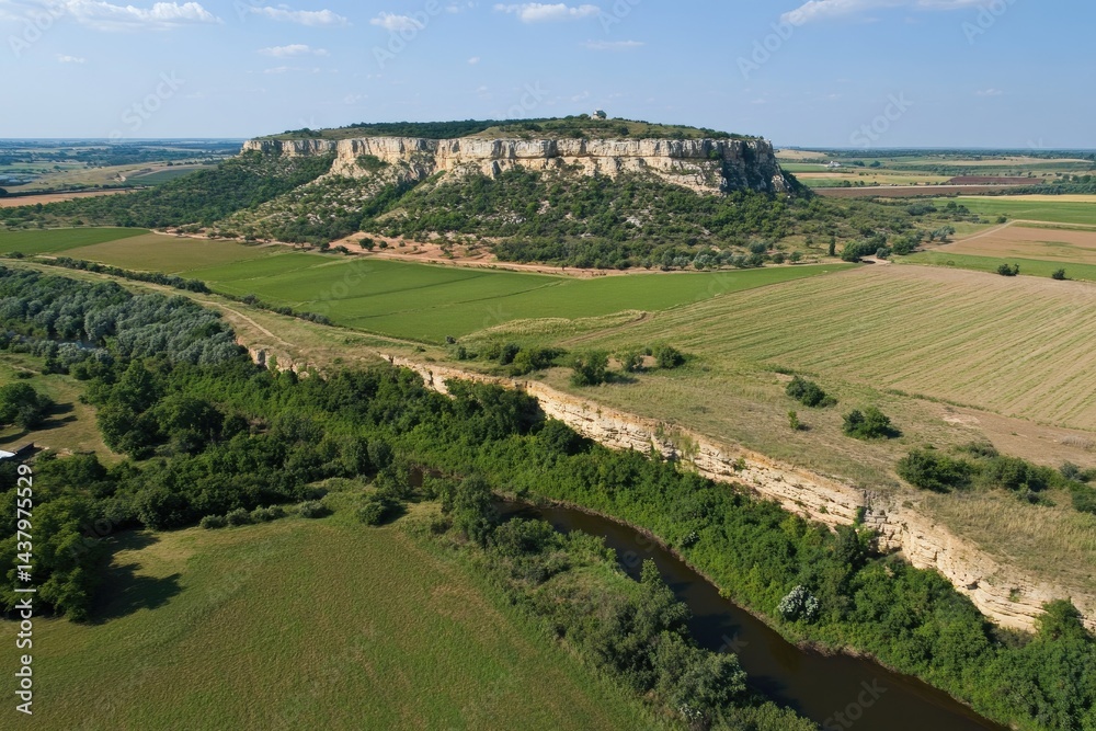 Naklejka premium High-angle view of a river winding through a landscape of farmland and a chalky mesa Fields of various crops, a meandering river, and a prominent, light-colored, flat-topped hill are visible